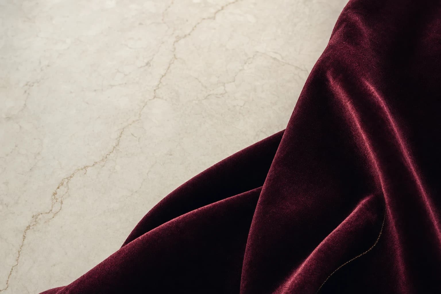Deep burgundy velvet folds on warm ivory stone